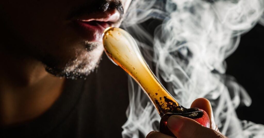 Photograph of man with goatee with a glass pipe smoking drug with smoke eminating from pipe. Autobiography of Notre Dame.