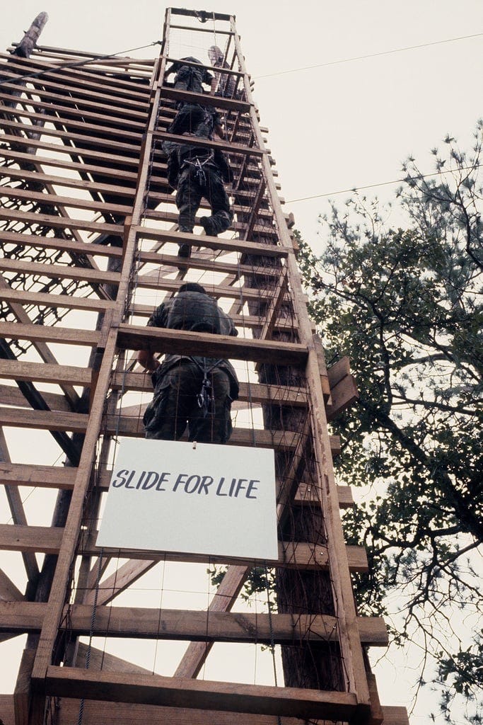 Cadets at ROTC Advance Camp climbing up wooden tower for the Slide For Life obstacle.  Biography of Dr. Anthony J. Carbone.