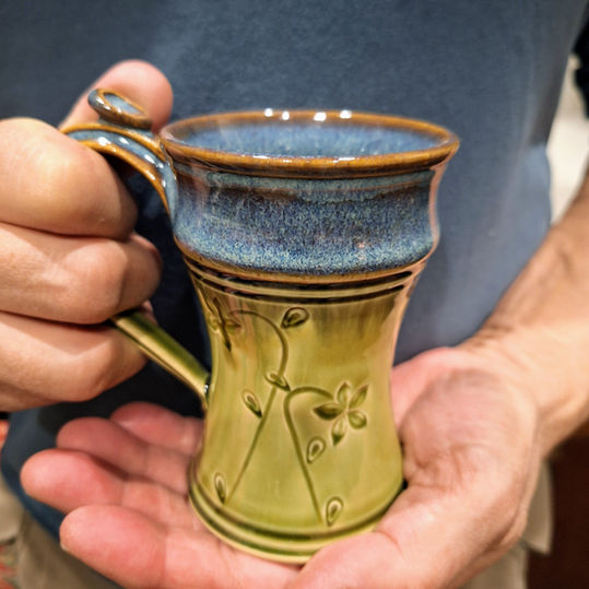 Close-up of hand-stamped botanical surface decoration on a wheel-thrown stoneware mug, showing original stamp design handmade at Plays In Mud pottery studio in West Asheville NC.