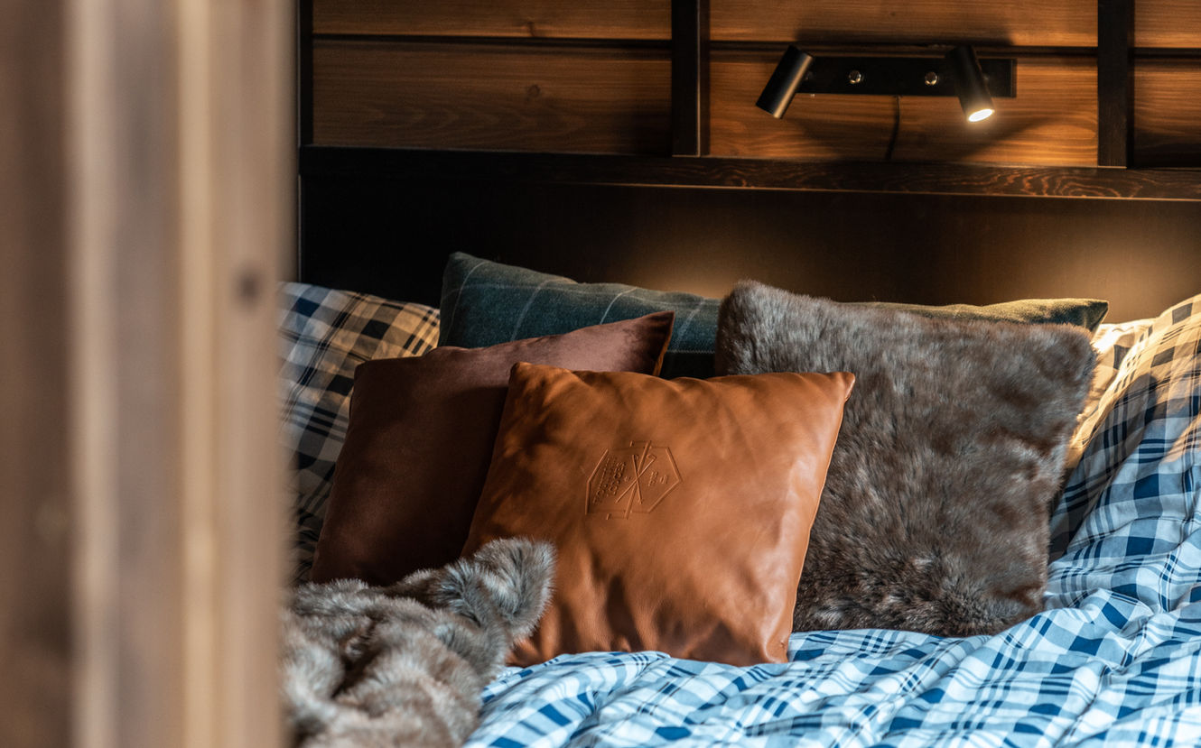 Sovrum med kuddar, sängkläder och ljus ovanför. Inredning i stuga, mysig atmosfär.