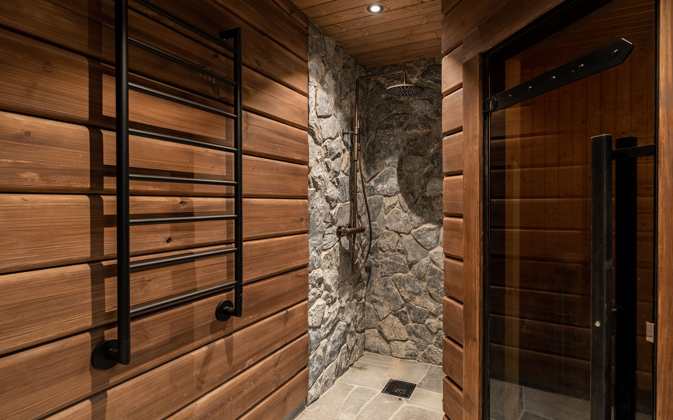 Modernt badrum med träväggar och dusch med stenbeklädnad och svart torkställning.