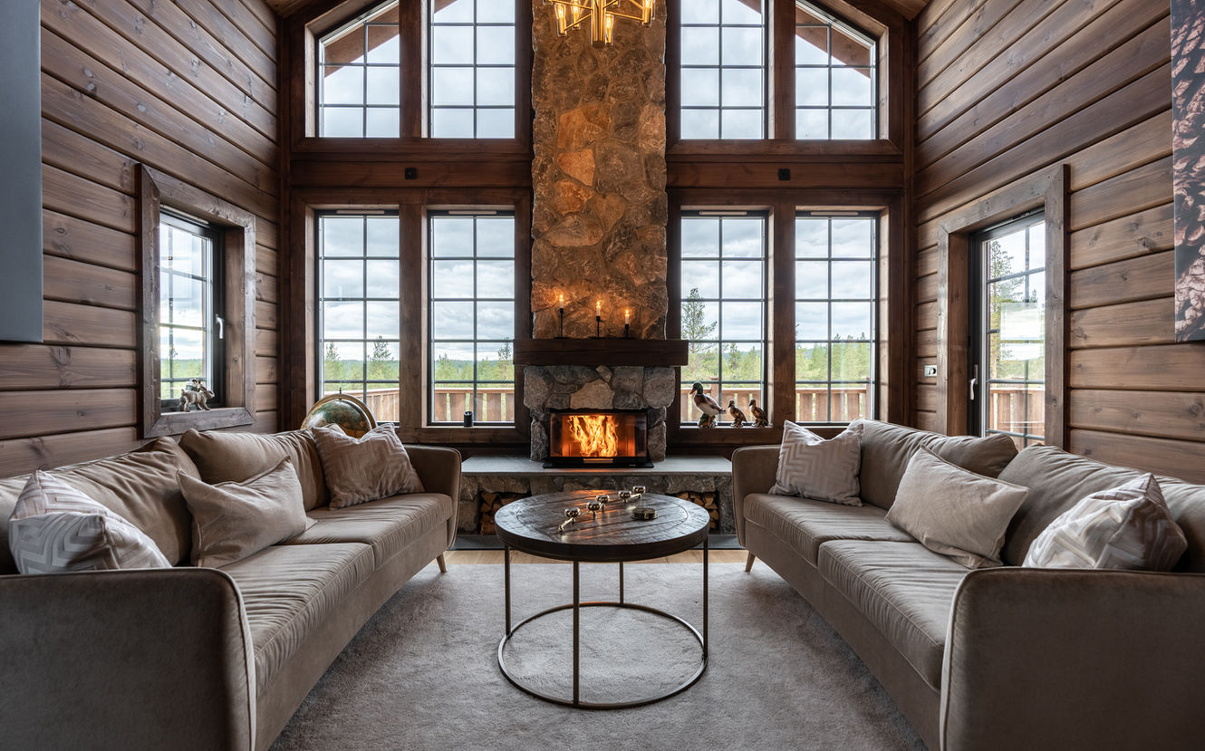 Vackert vardagsrum med öppen spis, två soffor och stora fönster, Fjällstugebyggarna.
