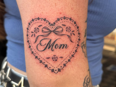 A fine-line "Mom" heart tattoo with floral adornments.