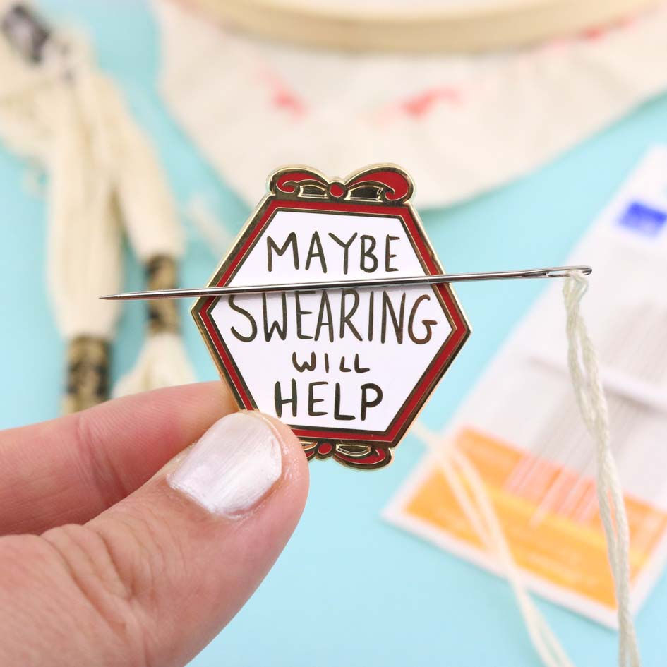 Thumbnail: A hexagonal enamel needle minder with a red and gold trim. The minder has the text 'MAYBE SWEARING WILL HELP' written in a wh
