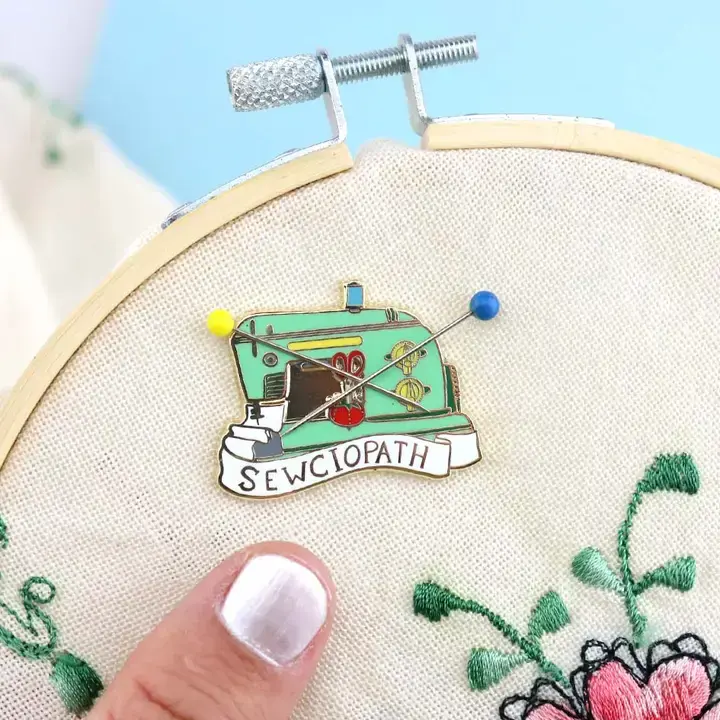Thumbnail: A green enamel needle minder with a 'Sewciopath' label, designed to look like a retro sewing machine with a magnetic closure.