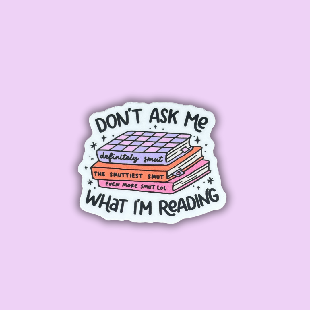 A sticker with an illustration of a book stack and text that reads 'DON'T ASK ME WHAT I'M READING' in various fonts and color