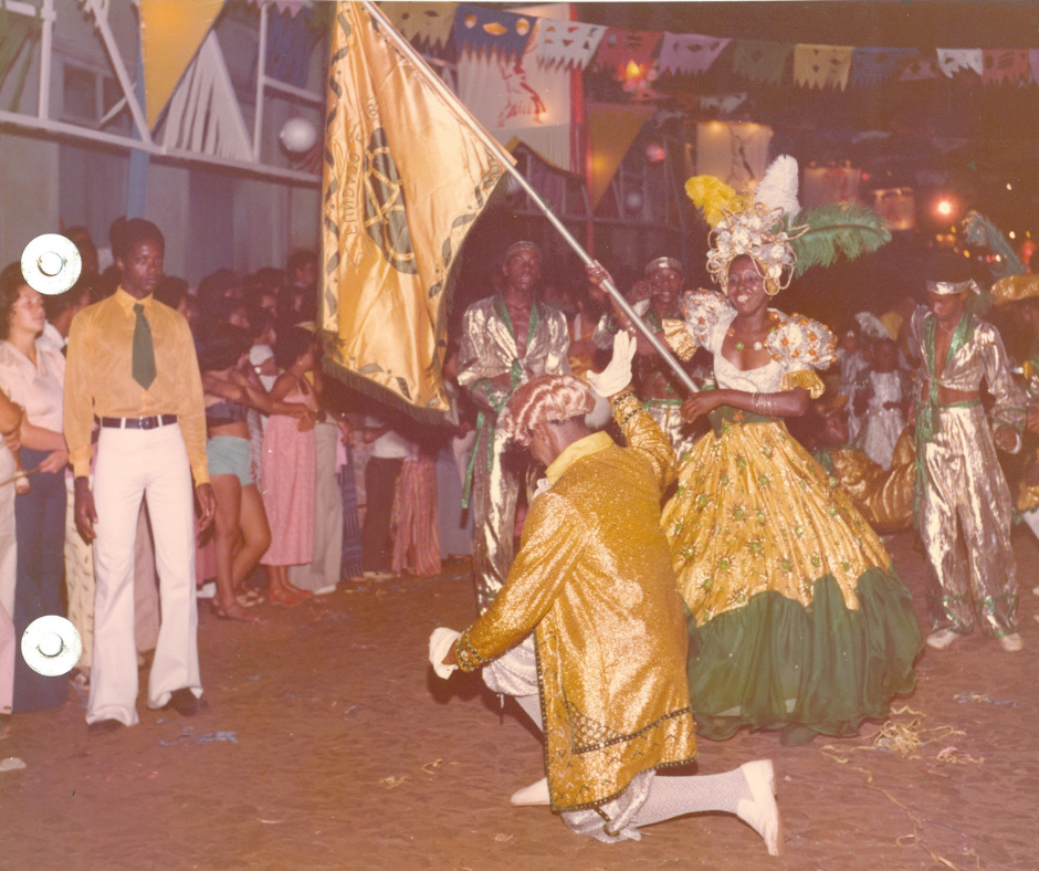 24- Clube Mundo Velho_ Foto antiga de desfile carnavalesco noturno destacando um homem neg
