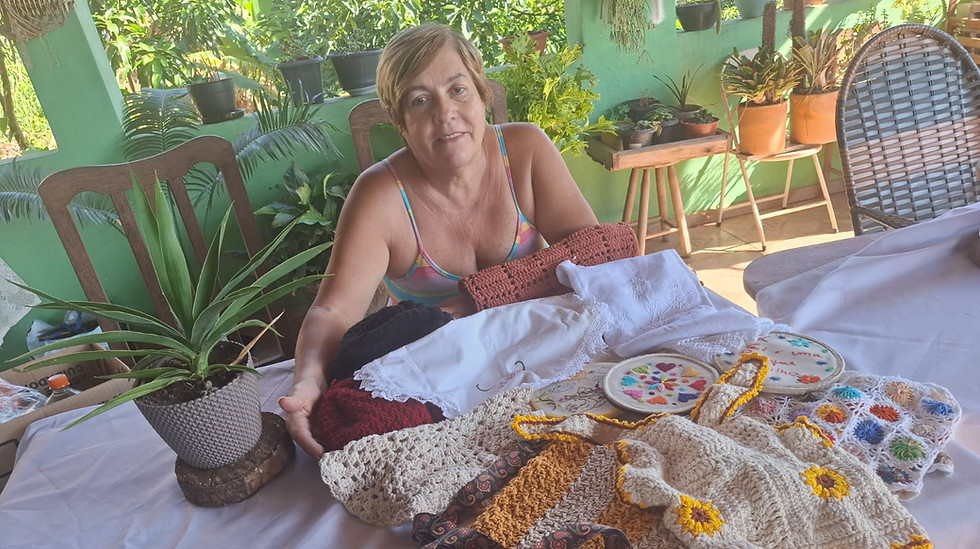 65- Artesã Merces Aparecida dos Santos: Mulher de pele branca sorridente, exibindo sobre u