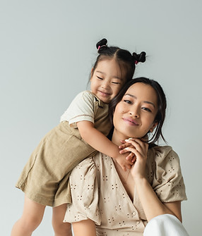 cheerful asian toddler daughter hugging happy mother isolated on gray.jpg