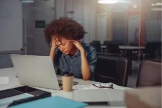 A solitary worker surrounded by an empty office space, absorbed in thought in front of a laptop, conveys a sense of isolation and fatigue.