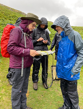 Three walkers in rain gear studying a map on a wet walk