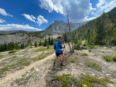 A hiker on a trail in the Beartooth wilderness, rugged mountain in the background, alpine view.