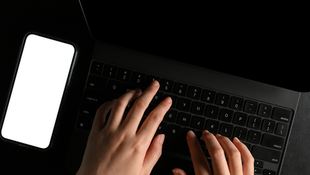 Top-down view of hands typing on a laptop keyboard next to a smartphone, illustrating the speed and privacy of digital journaling apps like Flammingo.