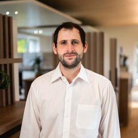 Ein Mann im weißen Hemd, lächelnd in einem Büro, Portraitaufnahme.