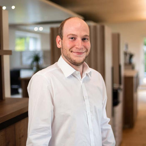 Ein lächelnder Mann in weißem Hemd, Portraitaufnahme in Innenräumen.