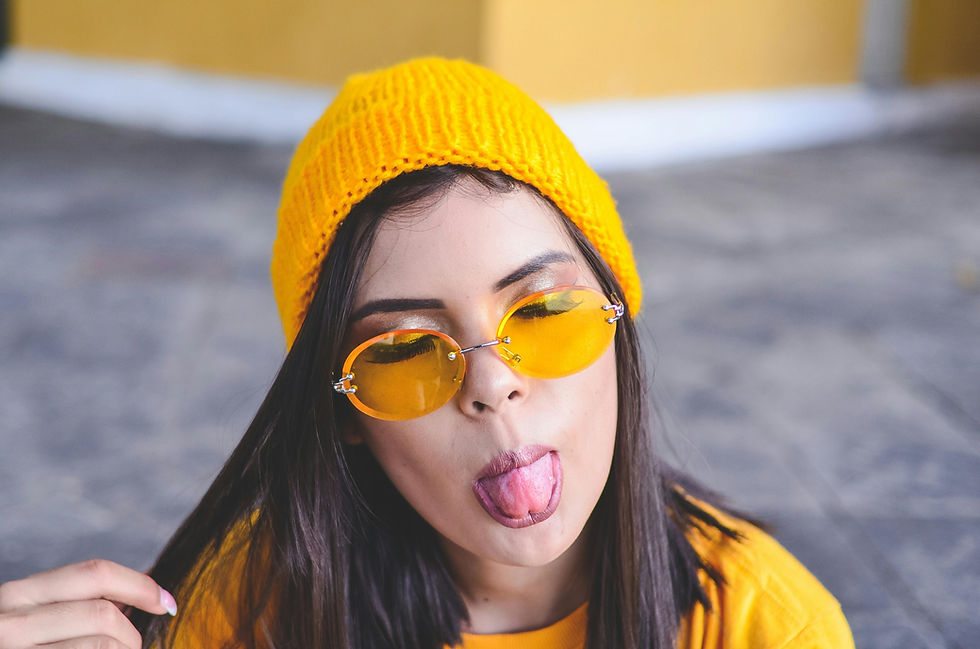 Playful young woman in casual streetwear with a yellow beanie and sunglasses, symbolizing that starting a streetwear brand in Europe is fun and not difficult.