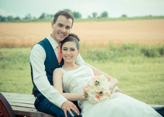 Photo of a husband and wife sitting on a wooden bench, smiling at the camera