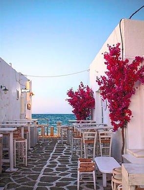 Charming street in Naousa, Paros, with white walls, magenta bougainvillea, and a path leading to the sea, capturing the idyllic setting of the Feminine Wholeness Retreat.