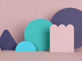 Colorful geometric paper shapes on a pastel pink background. Shapes include blue circles, a triangle, and a scalloped pink rectangle.