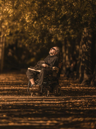A man with beard wearing sunglasses sitting in a wheelchair next to woodland