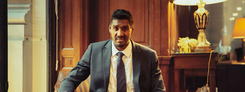 Un homme en costume assis pointe des cartes à jouer dans une pièce