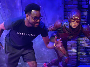 Man in black shirt pretending to race a wax statue of The Flash.