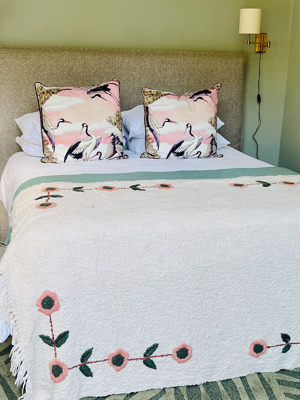 Small bedroom, queen bed with linen headboard, green leafy rug, cushions with storks, cream throw with pink and green embroidered flowers