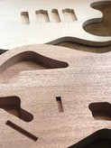 Back and top - a mahogany electric guitar back lies next to a book matched flame maple guitar top. The top and back have cavities which are partially complete