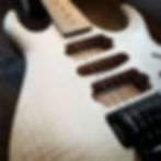 The image is a close up of the bare wooden body of an electric guitar and tremolo system. The guitar is incomplete and has no pickups installed, but has strings