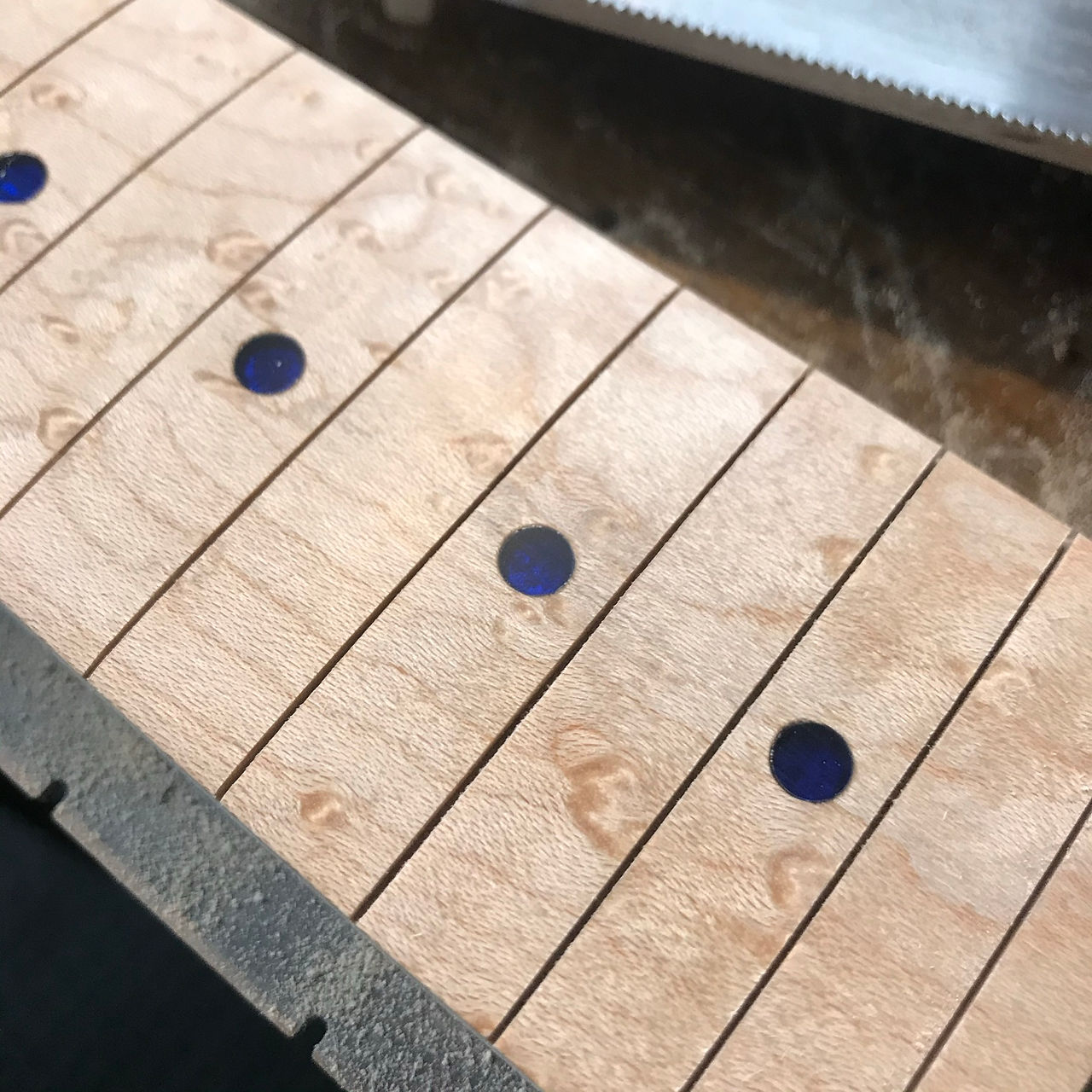 Fret makers - blue acrylic Inserting fret markersLocating the fret markers -  the image shows a partially completed Malone Guitars electric guitar neck. The neck is made from birds eye maple. Pencil marks show the centres of the fret dots. The fret markers are made from transparent blue acrylic