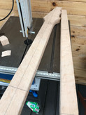 Cutting the neck blank - a guitar neck blank cut from a board of birds eye maple. It is laying on the table of an electric bandsaw