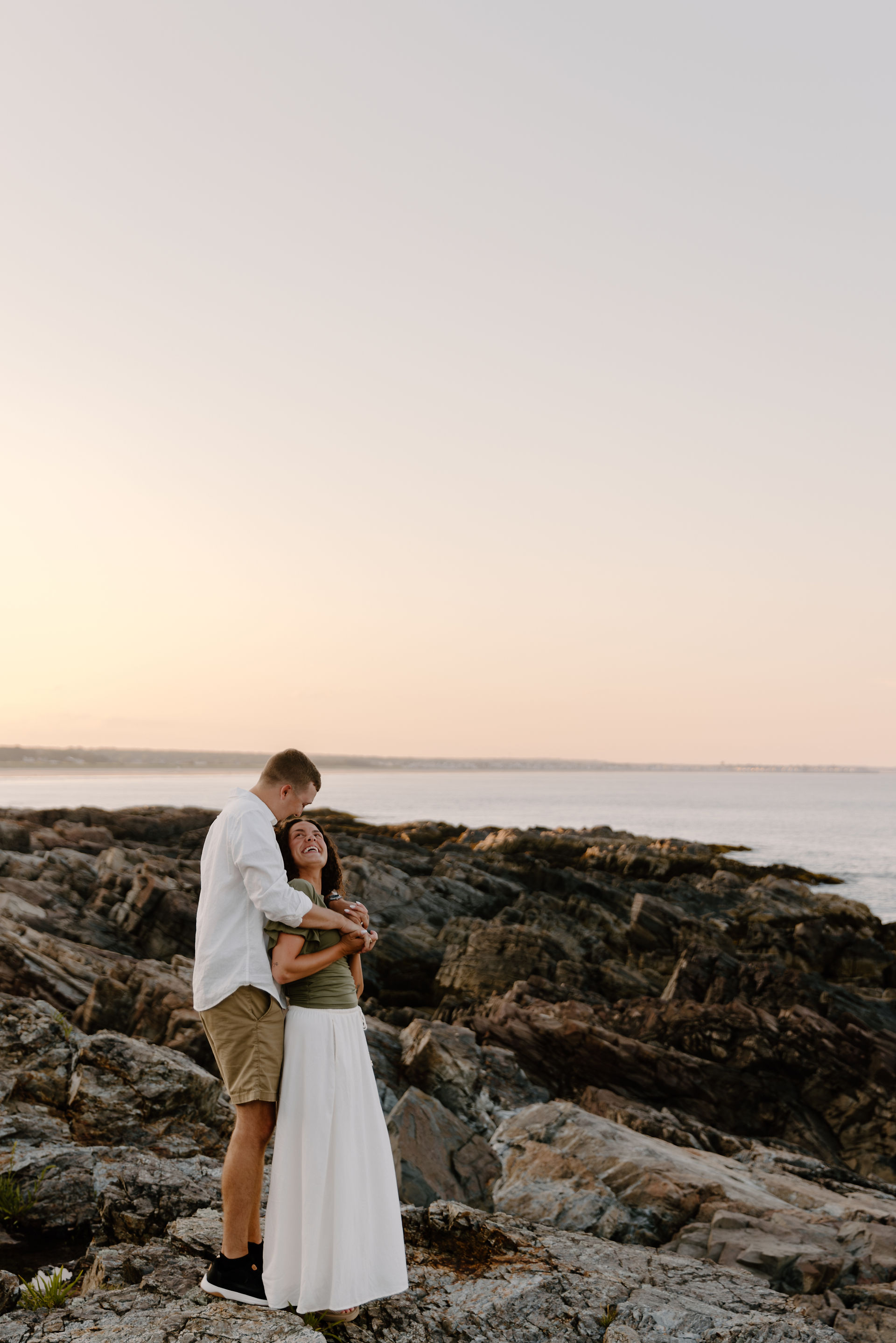couple hugging on rocks in Ogunquit Maine during coastal sunset photoshoot