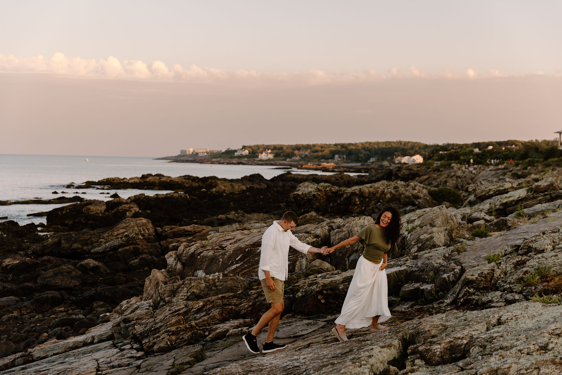 Girl leading boy up rocks in Ogunquit Maine during coastal sunset photoshoot