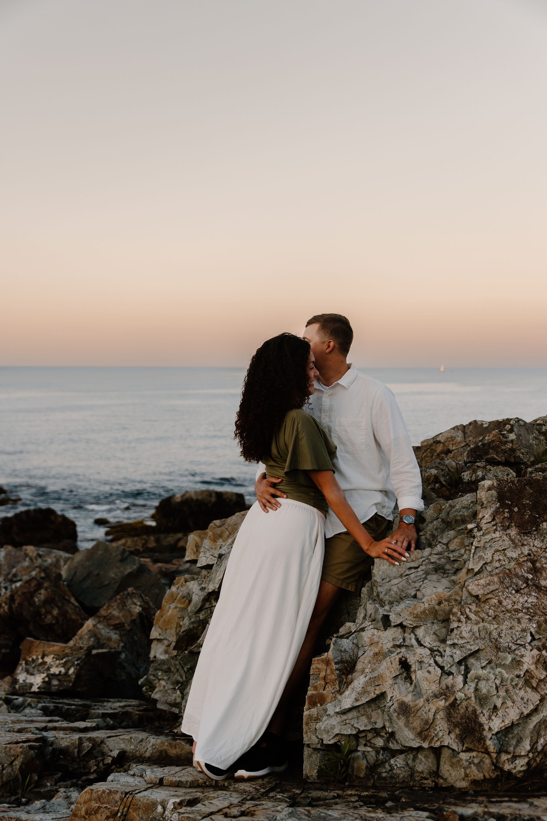 Couple posing on rocks during coastal engagement session in Ongunquit Maine during sunset