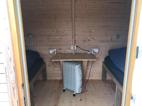 Sleeping hut from inside: showing two single beds and a small table with a heater below.
