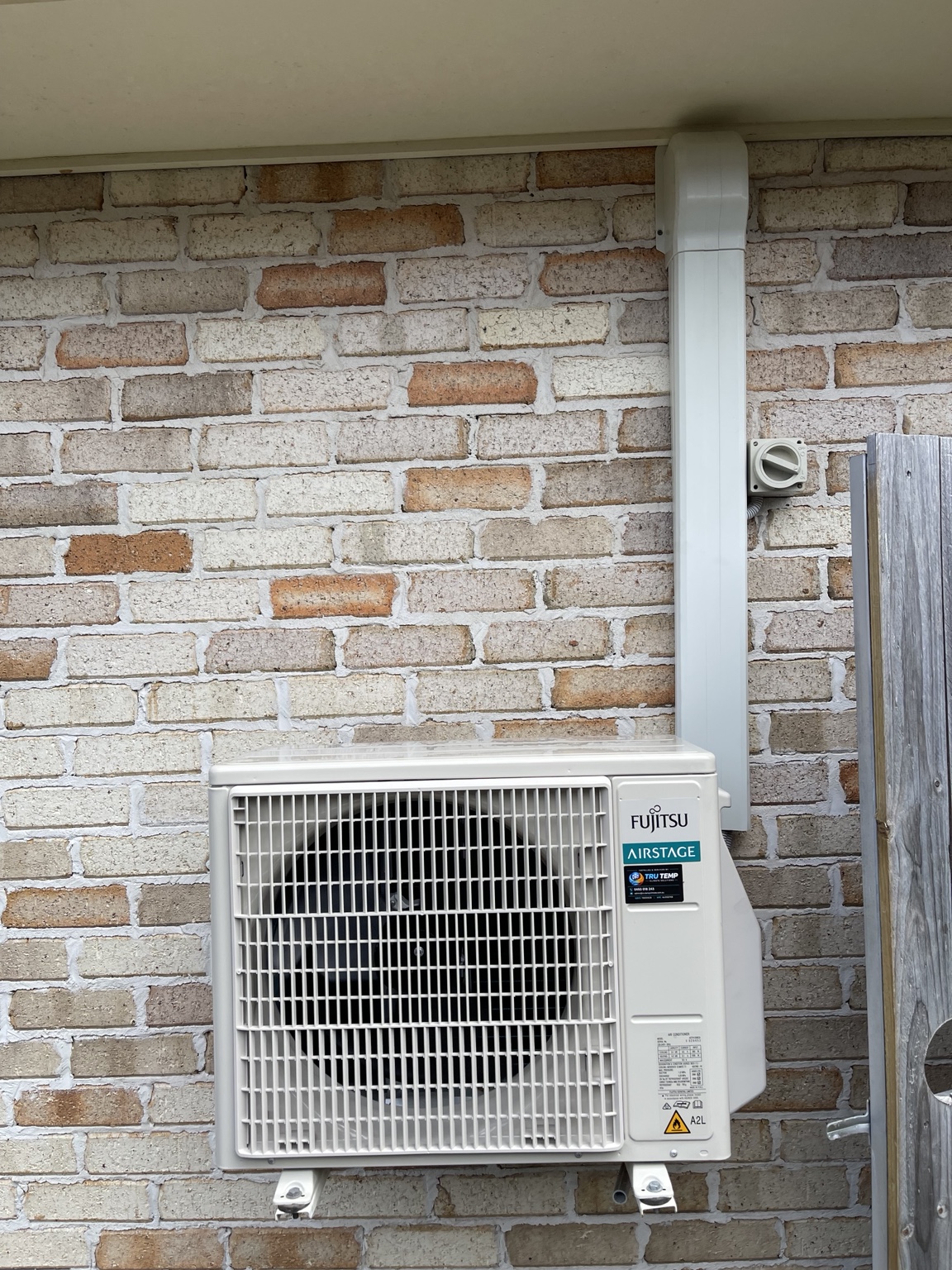 Outdoor air conditioner mounted beside a brick wall