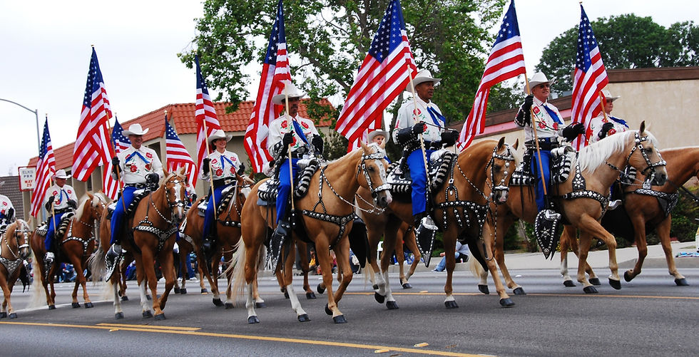 People dressed in uniforms riding horses carrying American flags.