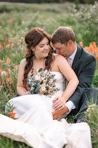Banff elopement photographer capturing the groom kissing the bride as she holds her bouquet while they sit in the meadows