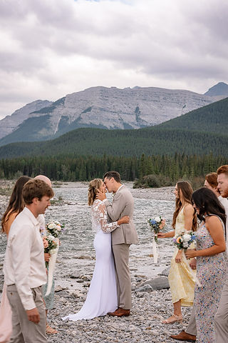 Bride and groom kissing while the wedding party gathers together near their Kananaskis wedding
