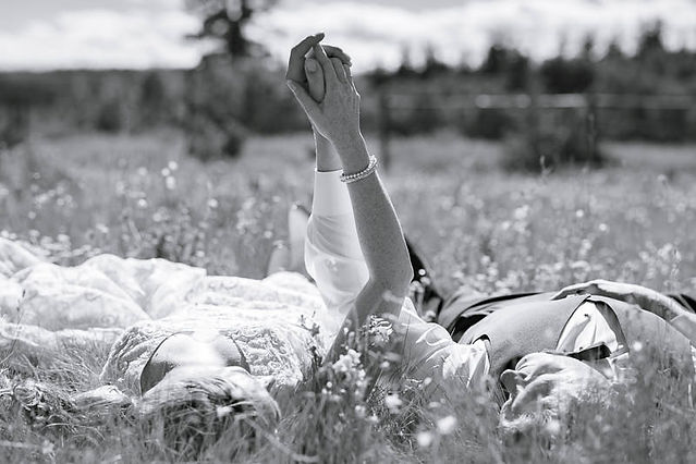 Bride and groom lying together in the grass holding hands and smiling in a black and white portrait at one of the beautiful Cochrane wedding venues.
