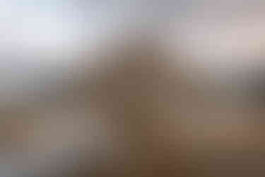 A couple walks hand in hand along the rocky shore of Bow Lake, their reflection visible in the still water beneath a dramatic, cloud-filled sky.