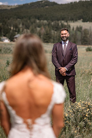 Bride standing with her back to the camera facing the groom in a grassy field  on their  Crowsnest Pass Wedding day 