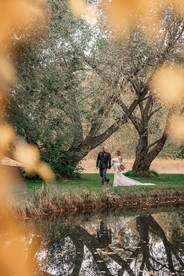 Strathmore photographer capturing a romantic bride and groom portrait beside a reflective pond surrounded by towering trees and soft autumn leaves during a countryside wedding.