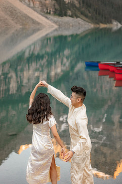 A bride and groom twirl together by the turquoise shoreline during their summer Moraine Lake wedding with mountain reflections behind them