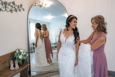 Mom smiling while she looking at her mom in her wedding dress, mother of bride holding the train of the wedding dress. reflection of them in full length mirror
