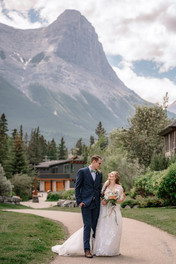 Bride and groom walking hand in hand during their Canmore Nordic Centre wedding, with towering Rocky Mountain peaks and beautiful alpine scenery creating a breathtaking backdrop.