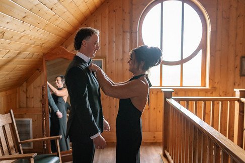A woman helping the groom with his suit while getting ready at a Coutts Centre wedding.