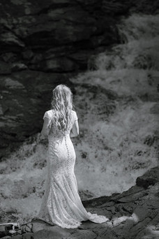Bride standing alone beside a waterfall in a rocky canyon on their Crowsnest Pass wedding day