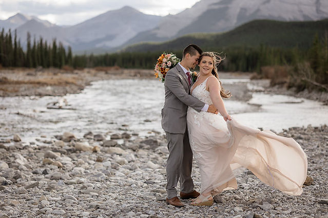 Landscape shot of brides dress flowing in the wind with groom looking at her