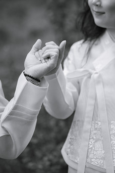 A black and white close-up of a couple holding hands, with the woman partly visible in frame, smiling softly as she looks toward her partner, capturing an intimate and timeless moment.